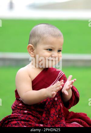 Un simpatico bambino calvo è vestito in avatar Monk, indossando uno scialle di maroon e dando un sorriso carino Foto Stock