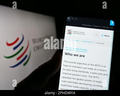 Persona che tiene il cellulare con la pagina web dell'Organizzazione Mondiale del Commercio (WTO) sullo schermo davanti al logo. Messa a fuoco al centro del display del telefono. Foto Stock