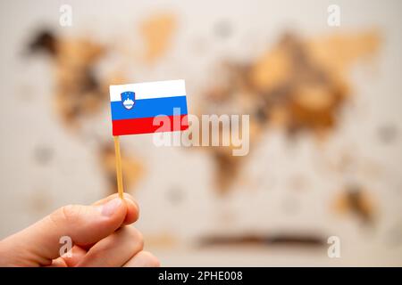 Bandiera Slovenia in mano mans sullo sfondo della mappa del mondo in legno. Economia globale e concetto geopolitico. Foto Stock