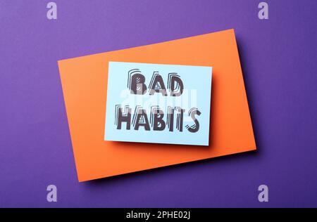 Nota cartacea con parole cattive abitudini su sfondo viola, vista dall'alto Foto Stock