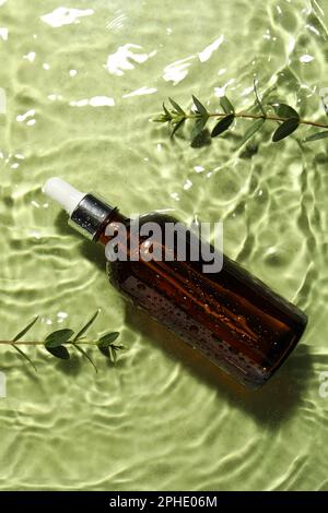 Bottiglia di olio idrofilo e ramoscelli di piante in acqua su fondo verde chiaro, piatto Foto Stock