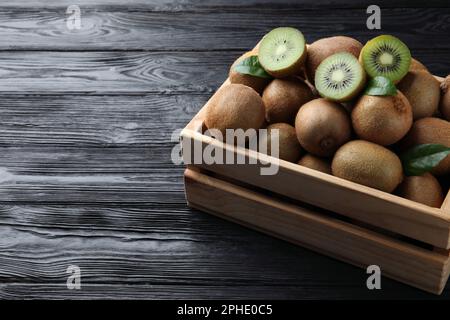 Cassa con taglio e kiwi interi freschi su tavola di legno nero, spazio per il testo Foto Stock