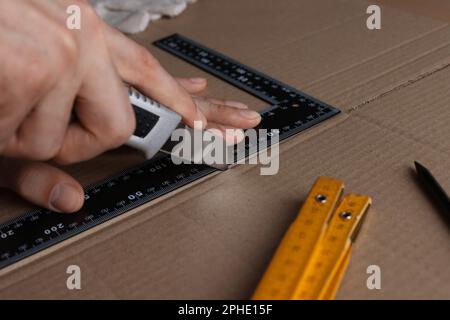 Uomo che taglia cartone con coltello e righello, primo piano Foto Stock