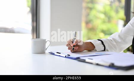 Immagine ravvicinata della mano di una donna d'affari che tiene la penna, scrivendo o firmando la sua firma su un documento aziendale alla sua scrivania. Foto Stock