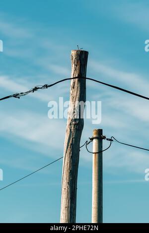 Due poli elettrici, uno in legno e uno in cemento con fili elettrici, focalizzazione selettiva Foto Stock