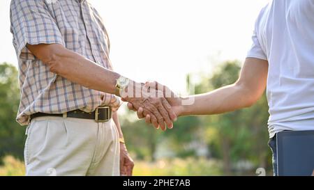 Immagine ritagliata di un uomo d'affari o di un fornitore che scuote le mani con un agricoltore anziano in un campo di mais, facendo un contratto agricolo, trattando affari. Foto Stock