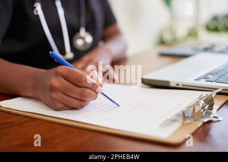 Primo piano shot di medico nero che riempie i sintomi del paziente sulla clipboard alla scrivania Foto Stock