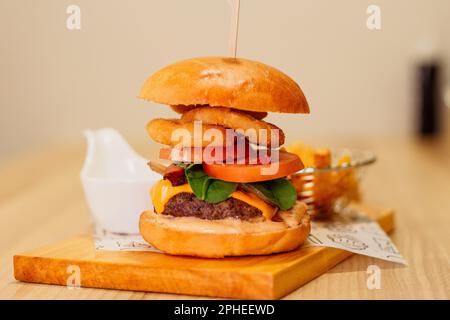 Un succoso hamburger tortino servito su un tagliere, sormontato da anelli di cipolla dorati Foto Stock