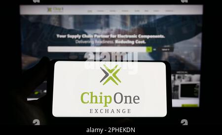 Persona che tiene uno smartphone con il logo della società di distribuzione tedesca chip 1 Exchange sullo schermo di fronte al sito Web. Messa a fuoco sul display del telefono. Foto Stock