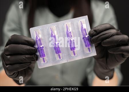 Attrezzi permanenti per il trucco nelle mani femminili. Aghi, trucco permanente, labbra, sopracciglia, maestra di trucco permanente, aghi e guanti monouso. Permanente Foto Stock