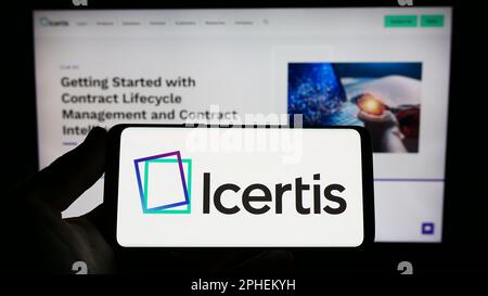 Persona che tiene in mano uno smartphone con il logo della società di software CLM statunitense Icertis Inc. Sullo schermo di fronte al sito Web. Messa a fuoco sul display del telefono. Foto Stock