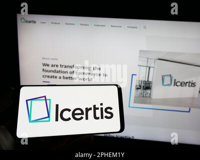 Persona che tiene il telefono cellulare con il logo della società americana di software CLM Icertis Inc. Sullo schermo di fronte al sito web. Messa a fuoco sul display del telefono. Foto Stock