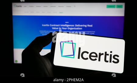 Persona che tiene il cellulare con il logo della società di software US CLM Icertis Inc. Sullo schermo di fronte al sito web aziendale. Messa a fuoco sul display del telefono. Foto Stock