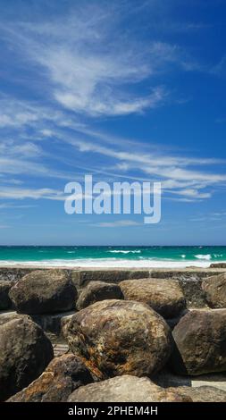 Si affaccia su una parete di cemento per una vista del mare e del cielo blu con nuvole spionate. Massi di roccia in primo piano. Snapper Rocks, Coolangatta. Foto Stock