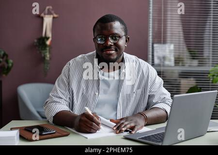 Immagine frontale di un uomo nero sorridente che indossa gli occhiali sul posto di lavoro in ufficio Foto Stock