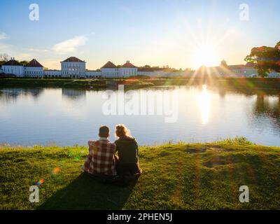 Coppia seduta in un canale vicino al Castello di Nymphenburg a Monaco durante il tramonto. Europa, Germania, Baviera Foto Stock