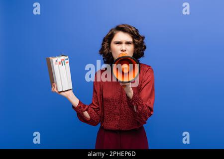 un insegnante di lingua rigoroso che tiene libri di testo e urla in megaphone isolato su blu, immagine di scorta Foto Stock