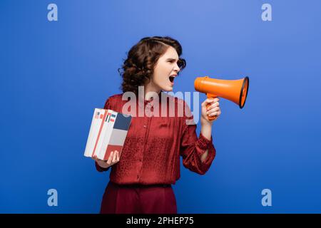 insegnante di lingue arrabbiato che tiene libri di testo e urla in megafone isolato su blu, immagine stock Foto Stock