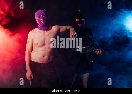 un uomo e una donna con il volto coperto in una stanza buia su sfondo nero Foto Stock