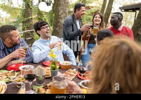 Famiglia e amici gustando un pranzo a casa, giovani persone multirazziali bere birra alla festa barbecue nel cortile del ristorante patio, concetto di frie Foto Stock