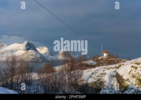 Handel und Verkauf von Øyfjorden und Schneebedeckten von Schneebedeckten von Senja, genannt Kongan und Skultraen. rotes Leuchtfeuer auf der Insel Husøy Foto Stock