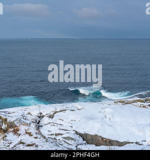 Vista panoramica sui fiordi e sulle ripide montagne innevate da Senja, Norvegia. Barca, pesci secchi, cespugli innevati e betulle sulla spiaggia. inverno Foto Stock