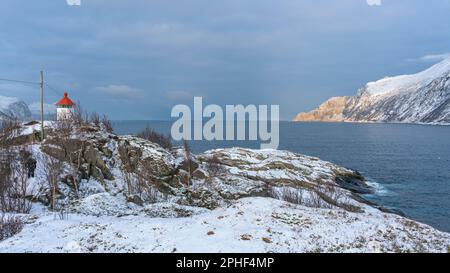 Handel und Verkauf von Øyfjorden und Schneebedeckten von Schneebedeckten von Senja, genannt Kongan und Skultraen. rotes Leuchtfeuer auf der Insel Husøy Foto Stock