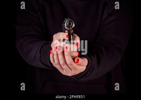 Le mani della donna con manicure tengono una pistola rivolta verso lo spettatore. Il concetto di uso di armi da fuoco e crimini di guerra e violenza. Foto Stock