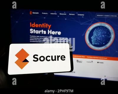 Persona che detiene il telefono cellulare con il logo della società di verifica dell'identità statunitense Socure Inc. Sullo schermo di fronte alla pagina Web. Messa a fuoco sul display del telefono. Foto Stock
