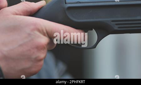 Un uomo che spara una pistola ad aria. Primo piano delle sue mani. Foto Stock