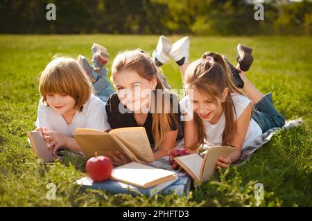 I bambini si posano in fila su erba verde e leggono libri nel parco dopo le lezioni scolastiche Foto Stock