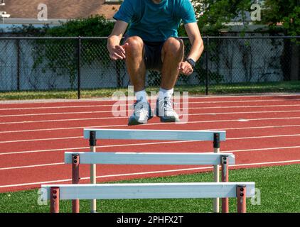 Ragazzo adolescente che salta sopra ostacoli pista per agilità e forza durante la pratica in pista e sul campo in estate. Foto Stock