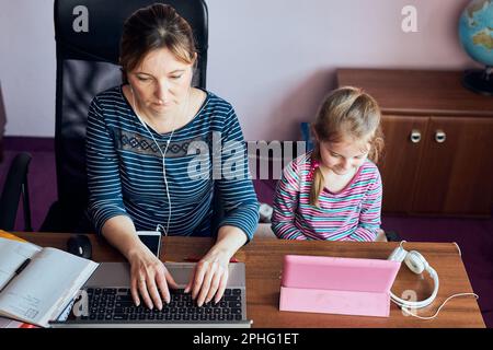 Donna madre che lavora in remoto durante il webinar del corso online di videochat sul laptop da casa mentre sua figlia guarda un video Foto Stock