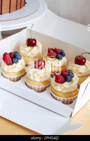 Primo piano su un set di cupcake decorati con frutti di bosco freschi, ciliegia, fragola e mirtillo in scatola regalo Foto Stock