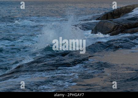 Am Fels sich brechende Wellen des Atlantik bei Tungeneset, Senja, Norwegen, mit den steilen Bergen Okshornan im Hintergrund. stürmisches Winterwetter Foto Stock