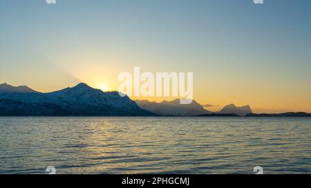 Abendrot mit einem hellen Sonnenstrahl über den verschneiten von Senja, Norwegen. Sandstrand im Winter am Ufer des Fjords bei Skaland, Troms Foto Stock