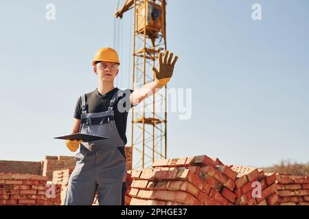 Mostra il segnale di stop a mano. Lavoratori edili in uniforme e attrezzature di sicurezza hanno lavoro in costruzione Foto Stock