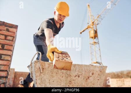 Tenendo mattone e usando martello. Lavoratori edili in uniforme e attrezzature di sicurezza hanno lavoro in costruzione Foto Stock