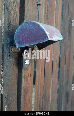 Lucchetto chiuso con coperchio in metallo che fissa il vecchio cancello di listelli in legno intemperiato Foto Stock