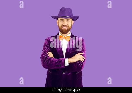 Studio ritratto di felice uomo bearded in cappello viola, tuta di velluto e cravatta arancio arco Foto Stock