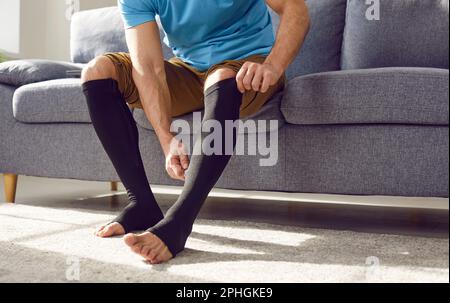 Uomo che mette su calze di compressione medica sulle gambe per la prevenzione delle vene varicose. Foto Stock