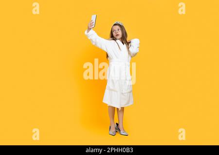 Little Girl in accappatoio, Crown e Mom's Shoes portare Selfie su smartphone Foto Stock