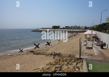 Odessa, Ucraina -2022: Barriere militari metalliche, ricci anticarro sulla spiaggia della città di mare. I vacanzieri si abbronzano accanto ai ricci anticarro in ferro. Recinzioni f Foto Stock