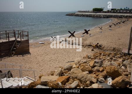 Odessa, Ucraina -2022: Barriere militari metalliche, ricci anticarro sulla spiaggia della città di mare. I vacanzieri si abbronzano accanto ai ricci anticarro in ferro. Recinzioni f Foto Stock