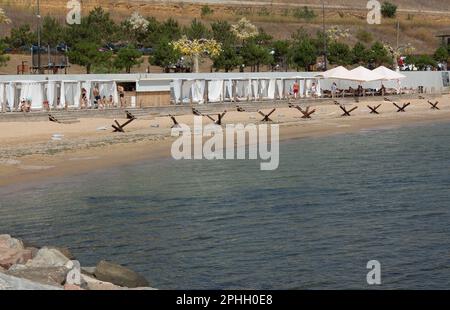 Odessa, Ucraina -2022: Barriere militari metalliche, ricci anticarro sulla spiaggia della città di mare. I vacanzieri si abbronzano accanto ai ricci anticarro in ferro. Recinzioni f Foto Stock