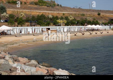 Odessa, Ucraina -2022: Barriere militari metalliche, ricci anticarro sulla spiaggia della città di mare. I vacanzieri si abbronzano accanto ai ricci anticarro in ferro. Recinzioni f Foto Stock