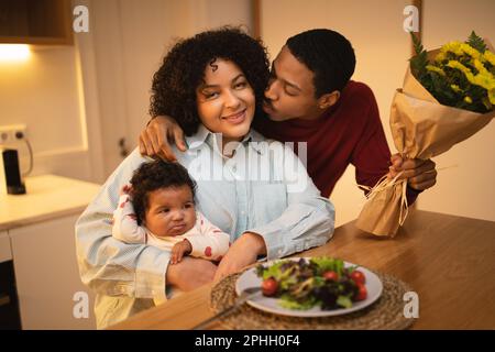 Amare il marito nero baciando la sua bella moglie che tiene il bambino Foto Stock