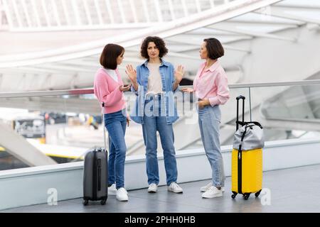 Tre amici femminili che discutono mentre aspettano al terminal dell'aeroporto Foto Stock