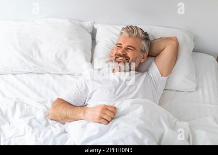 Vista ad angolo alto dell'uomo maturo positivo sdraiato a letto Foto Stock