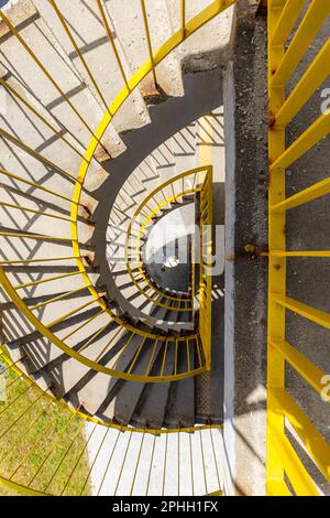 Vista dall'alto di una scala a chiocciola in cemento con ringhiere gialle in una mattinata soleggiata Foto Stock